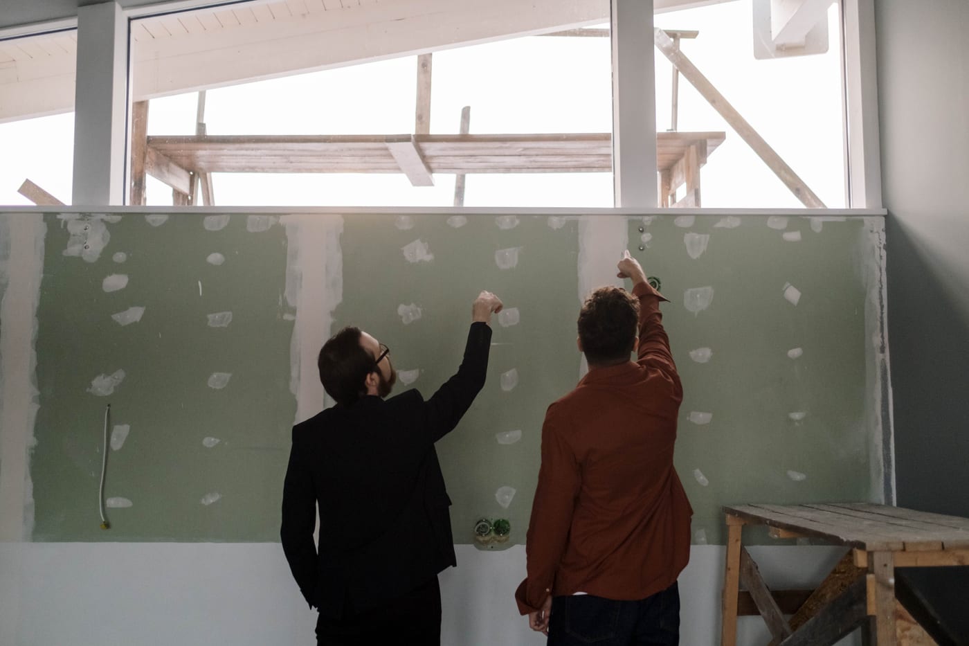 Zwei Trockenbauer verspachteln eine beplankte Wand unter der Dachkonstruktion